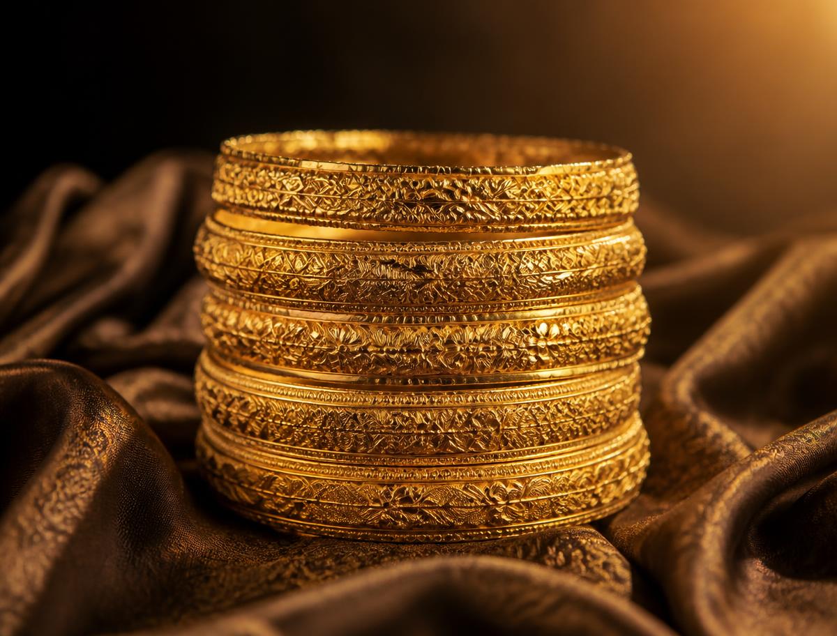 Stack of engraved 21K gold bangles on dark silk
